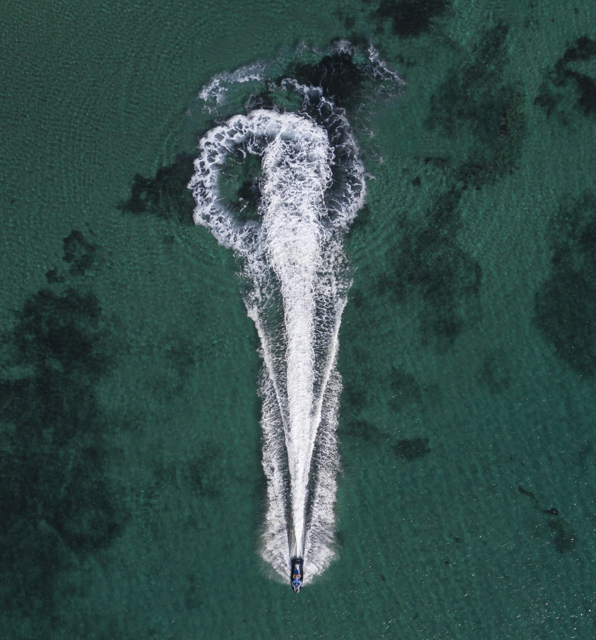 An aerial shot of a yacht cruising in the sea leaving splashing traces